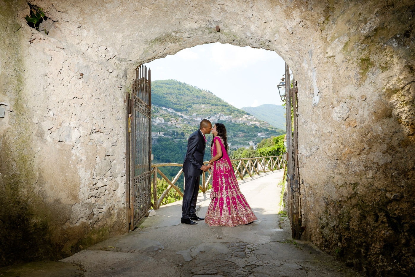 Bride and groom framed in an old stone archway in Ravello, looking out to the hills