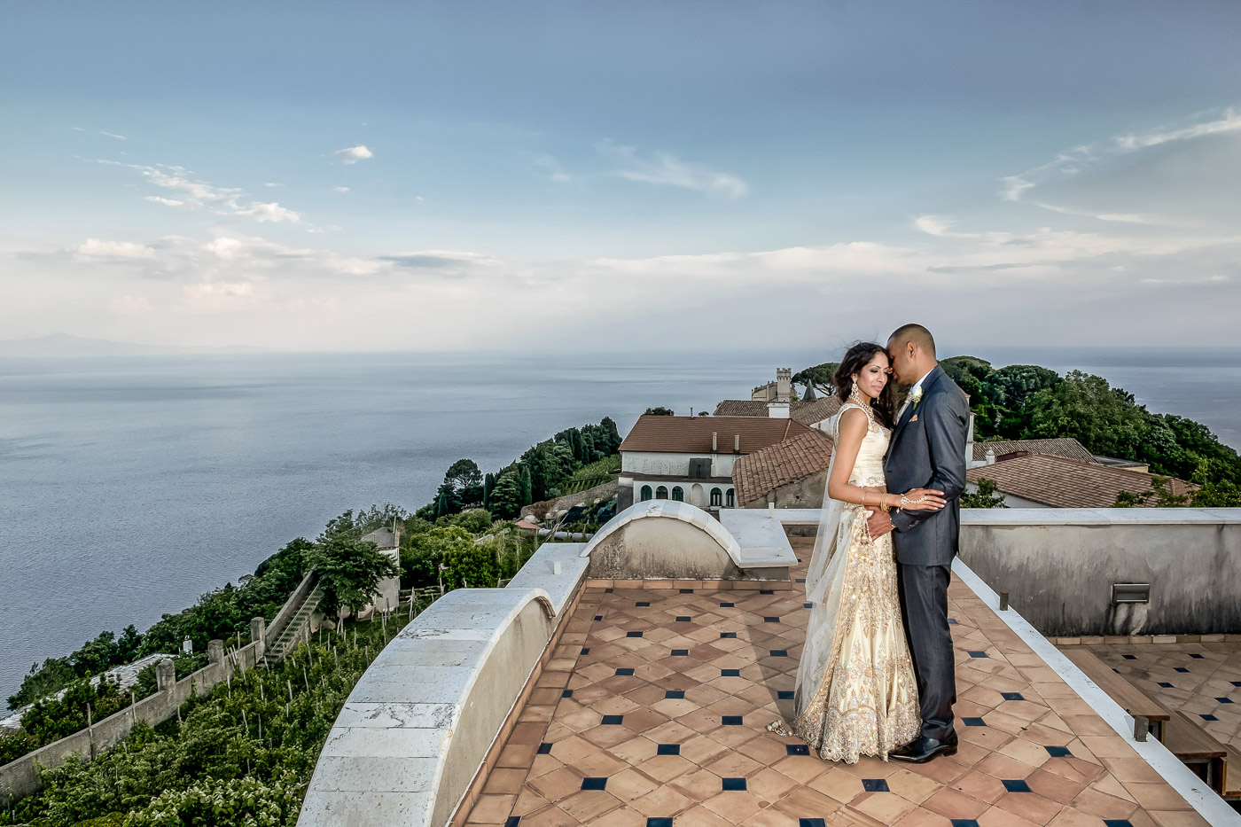 Bride and groom on a terrace high above the Amalfi coast at dusk, the sea behind them