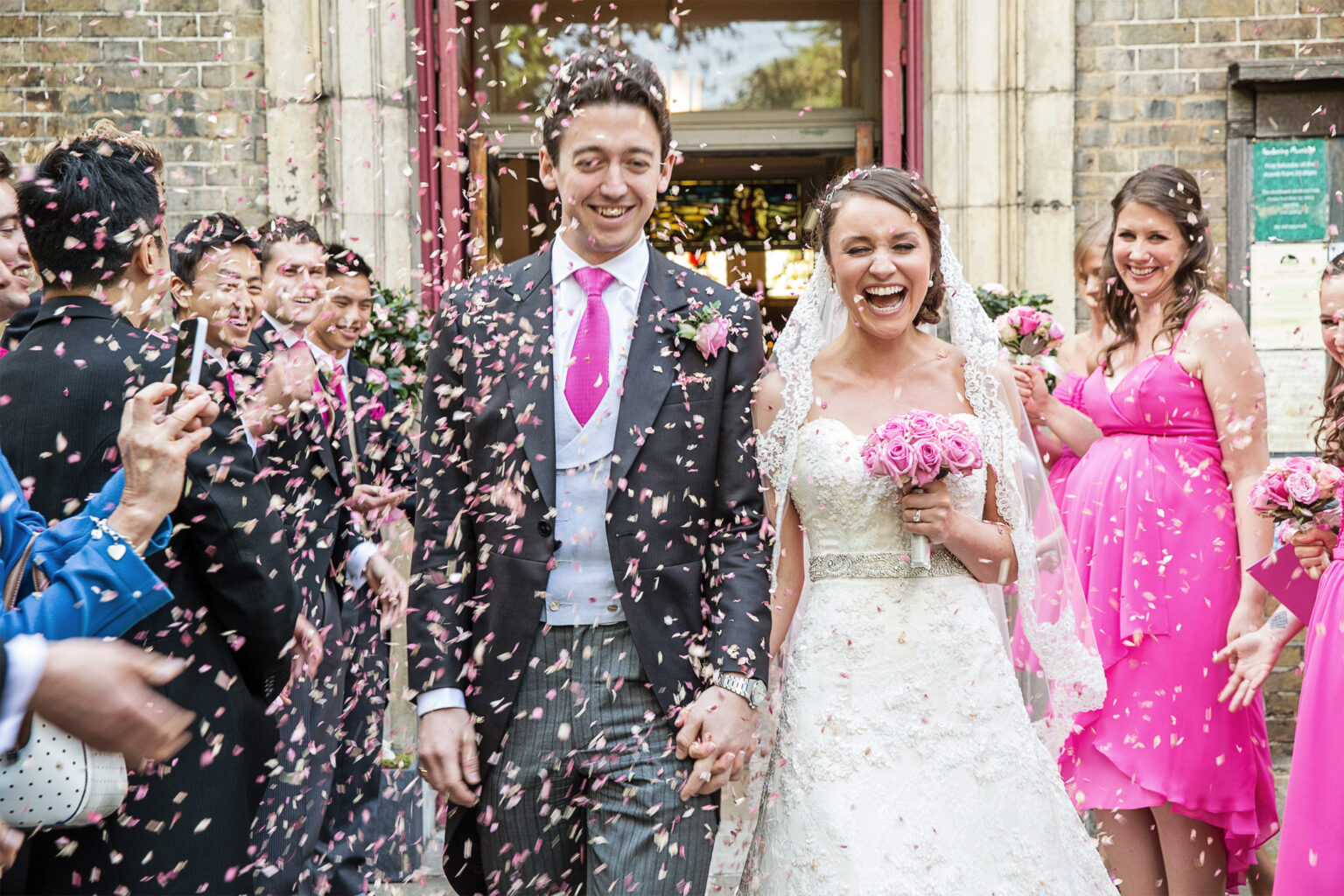 Guests throwing confetti over a laughing bride and groom outside their London wedding ceremony