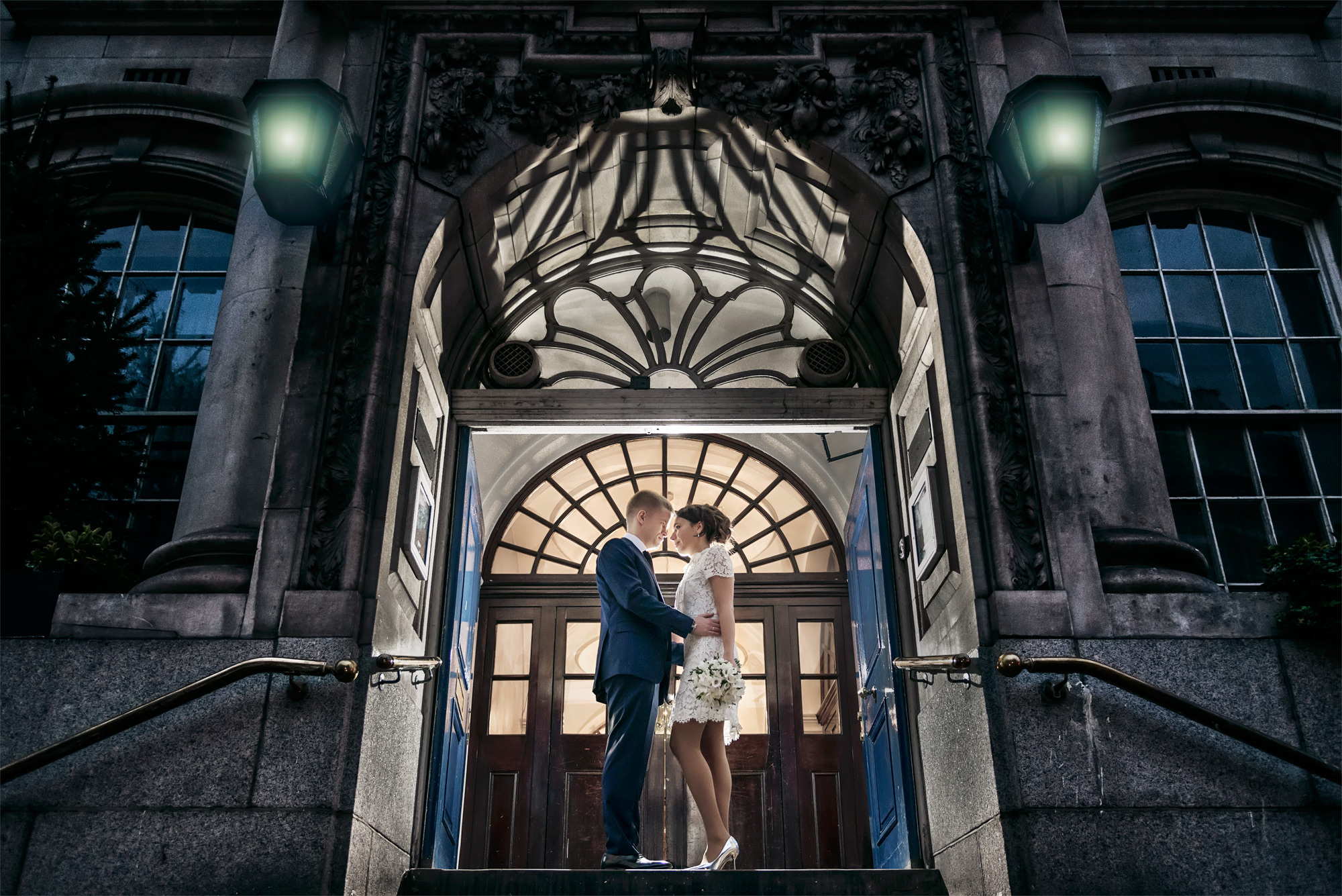 Bride and groom in the lit doorway of Chelsea Old Town Hall in the evening