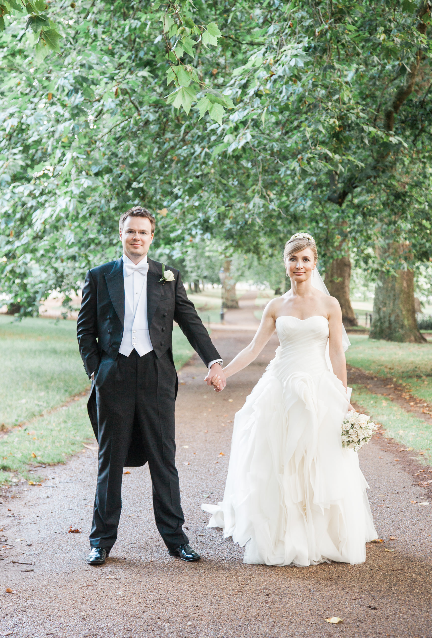 Bride and groom holding hands on a tree-lined path in Hyde Park near the Mandarin Oriental