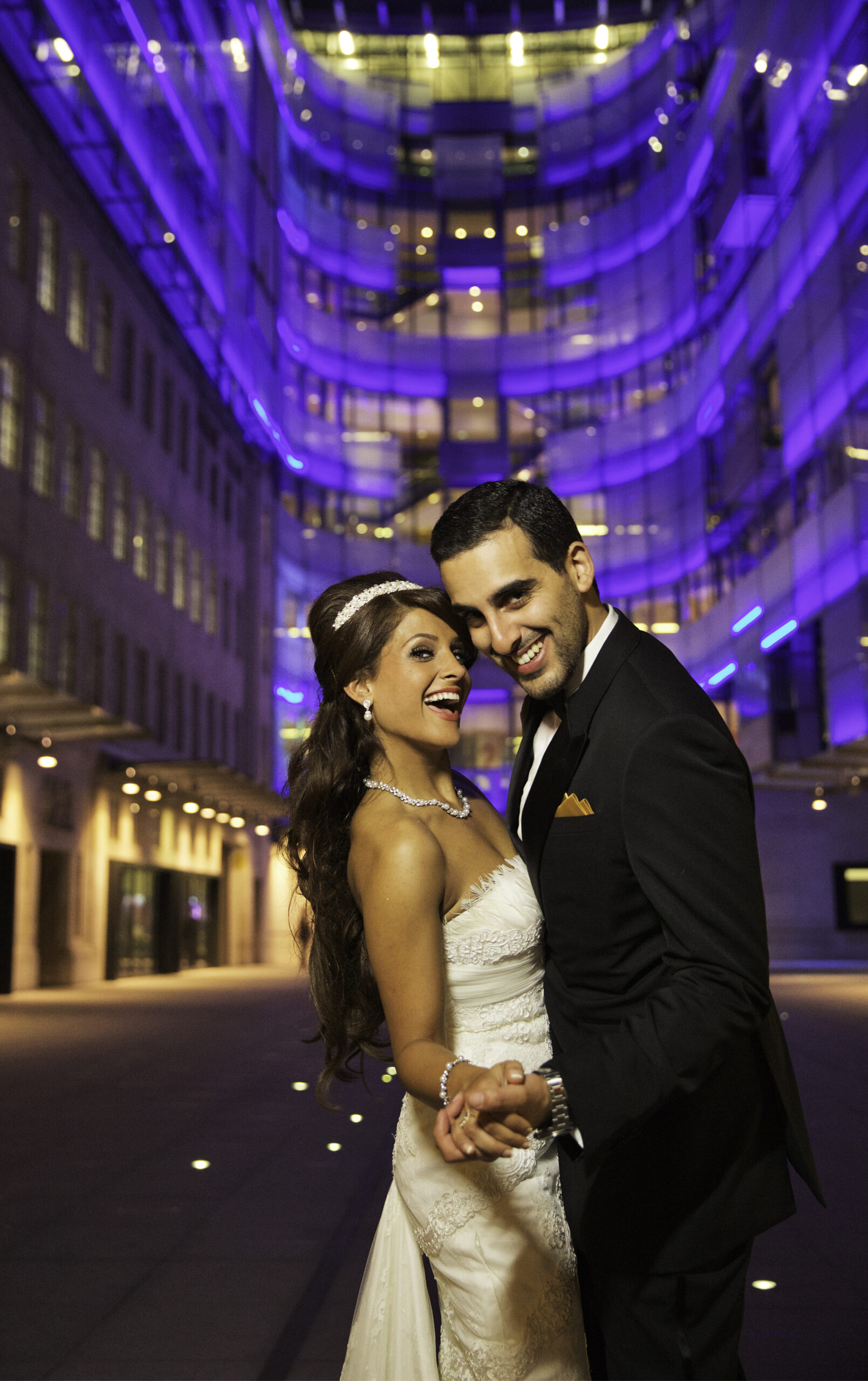 Bride and groom laughing at night outside BBC Broadcasting House, lit up in purple