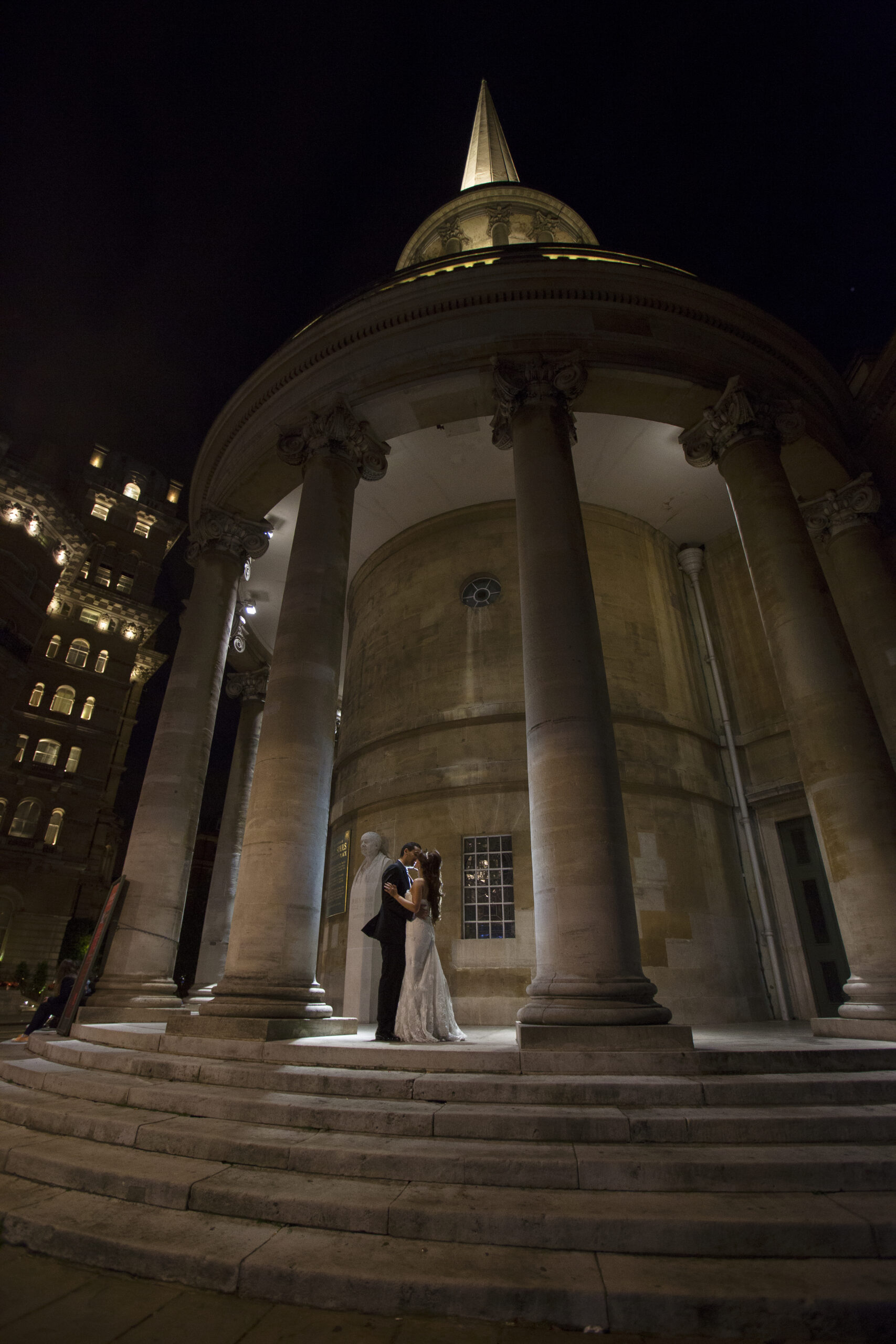 Bride and groom kissing between the columns of All Souls Church, Langham Place, at night