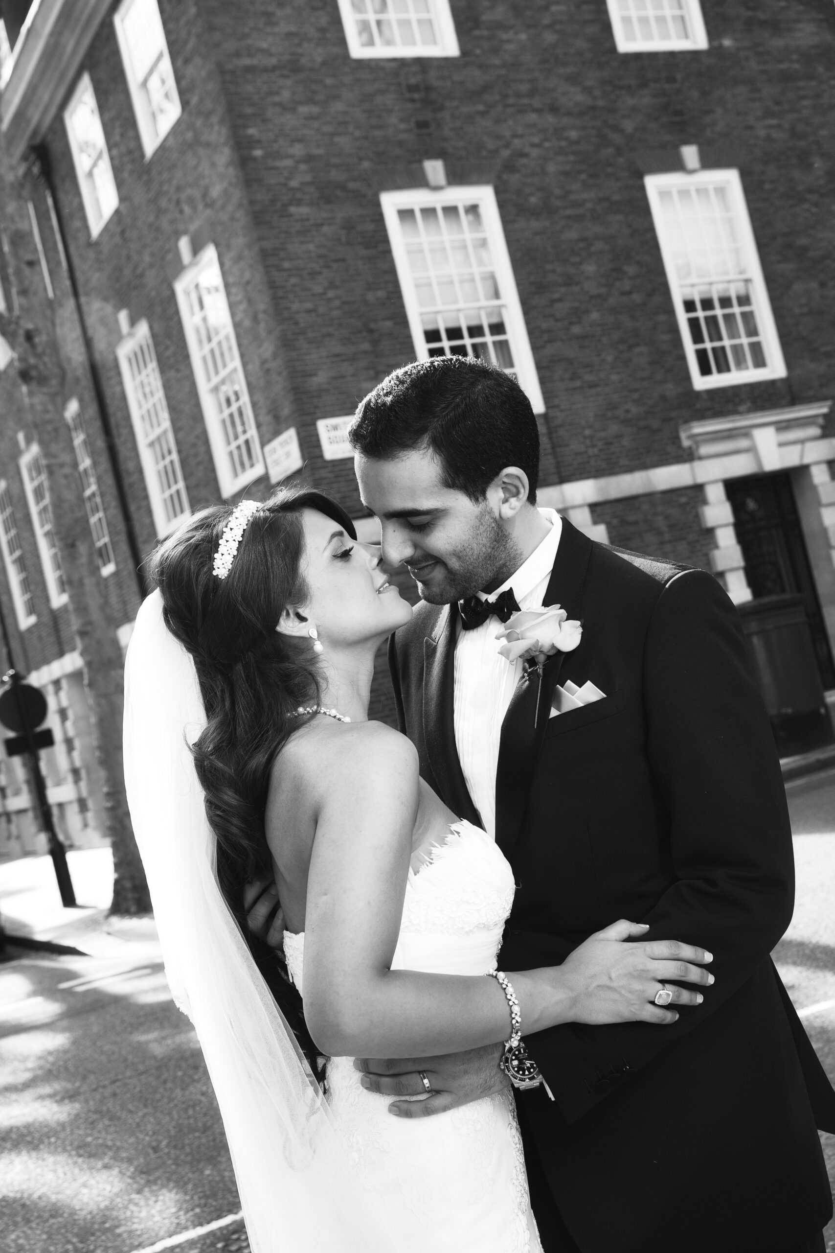 Black and white photograph of a bride and groom about to kiss on a street near the Langham