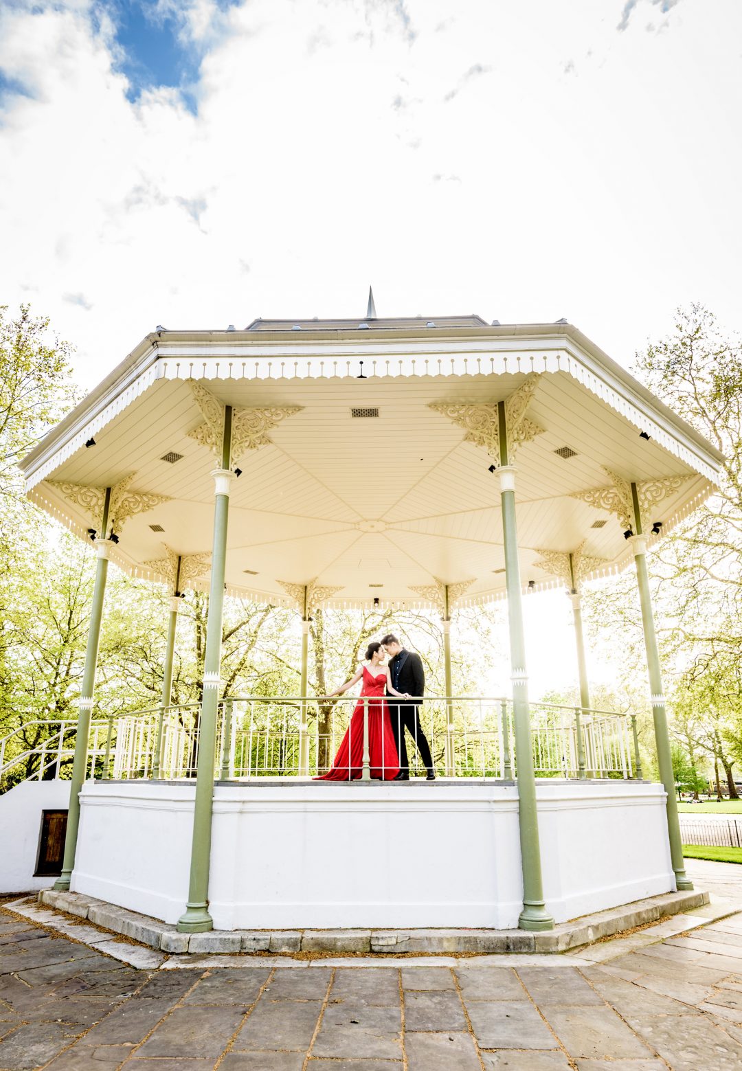 Bride in red gown and groom at the Hyde Park bandstand at the end of their London pre wedding shoot