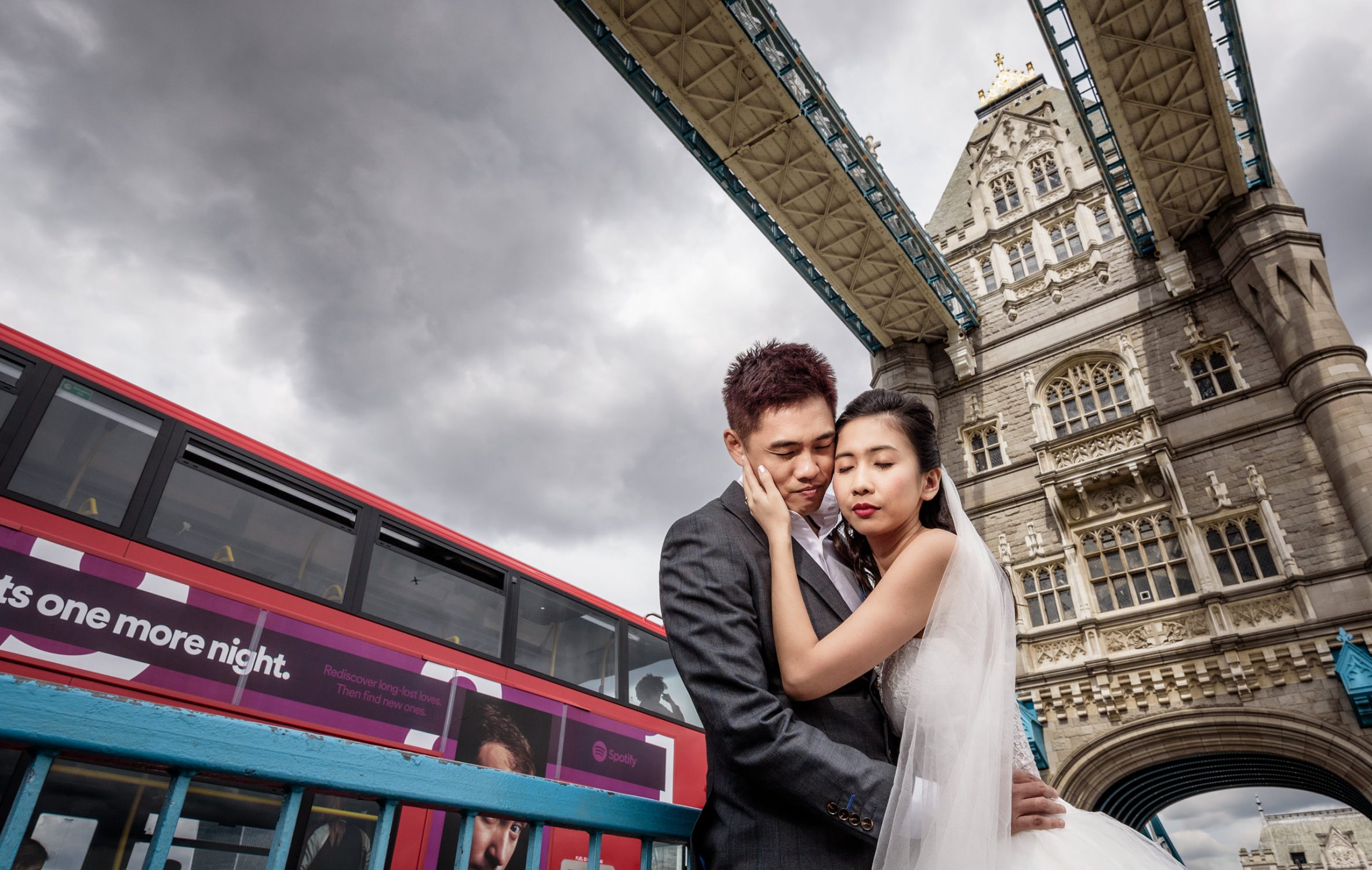 Couple embracing on Tower Bridge with a red London bus passing, London pre wedding shoot