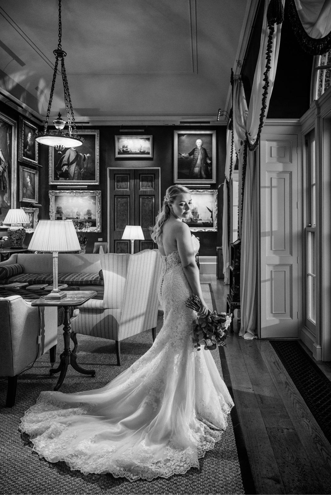 Bride in a long lace dress in a lamp-lit room at Goodwood House