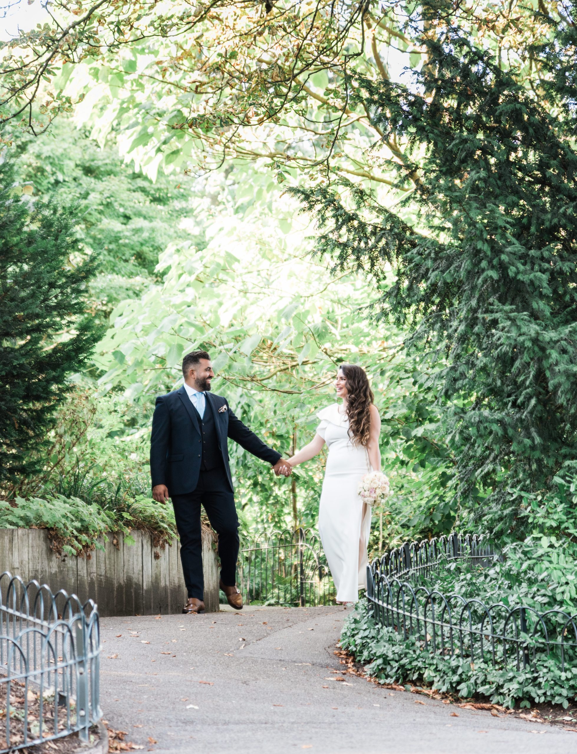 Bride and groom walking hand in hand along a leafy path in Regent's Park