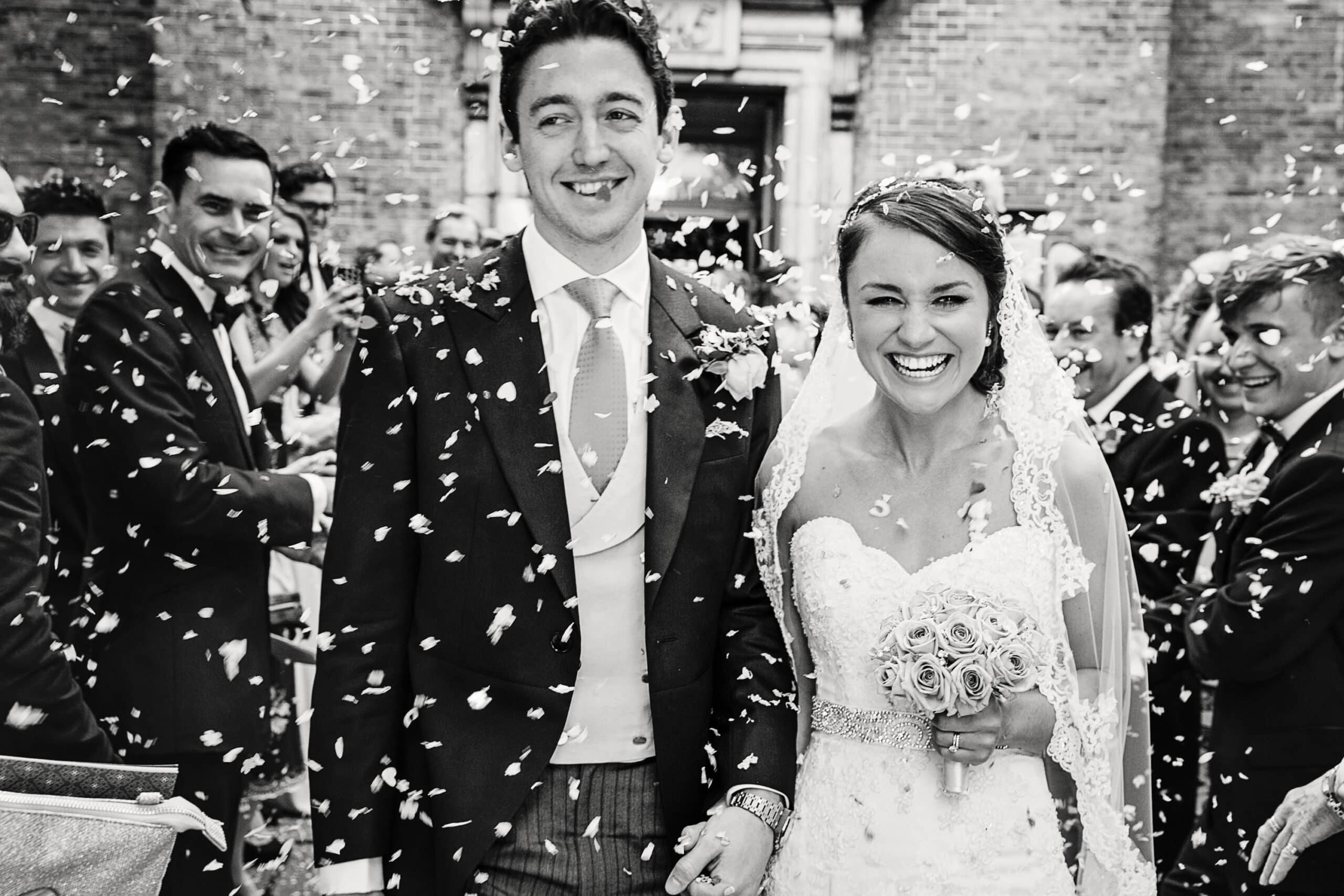 Black and white photograph of a bride and groom laughing through confetti