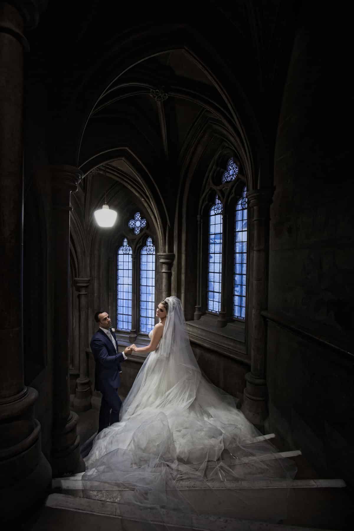 Bride and groom on a stone staircase by a Gothic window at the Royal Courts of Justice