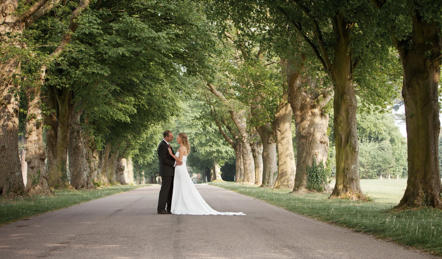 Bride and groom on the tree-lined avenue on the Goodwood Estate