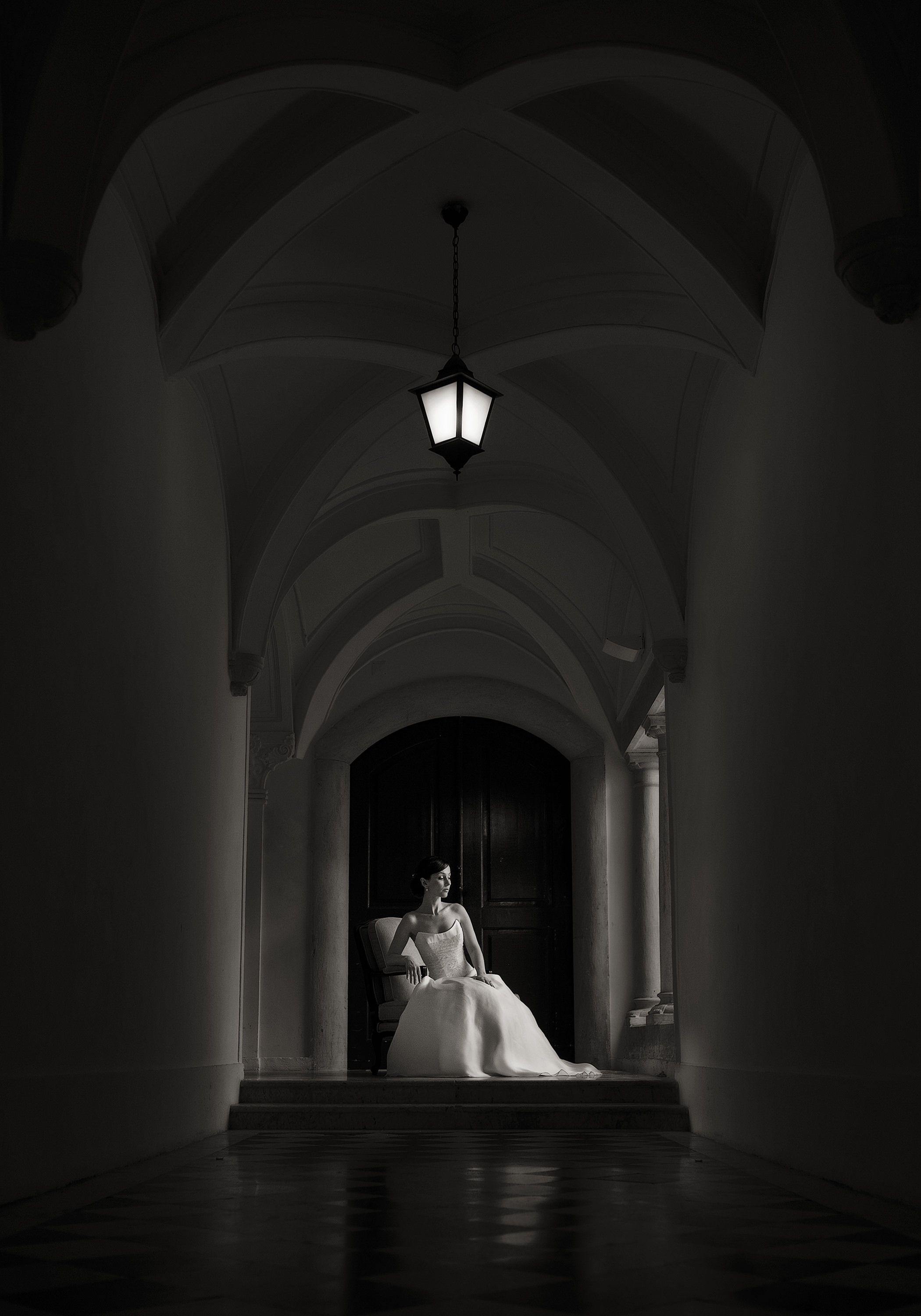 Black and white editorial wedding portrait of a bride at the end of a vaulted corridor