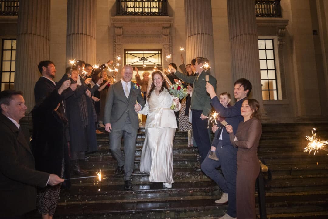 Nathalie and Rutger leaving Old Marylebone Town Hall down the front steps through a sparkler send-off after dark