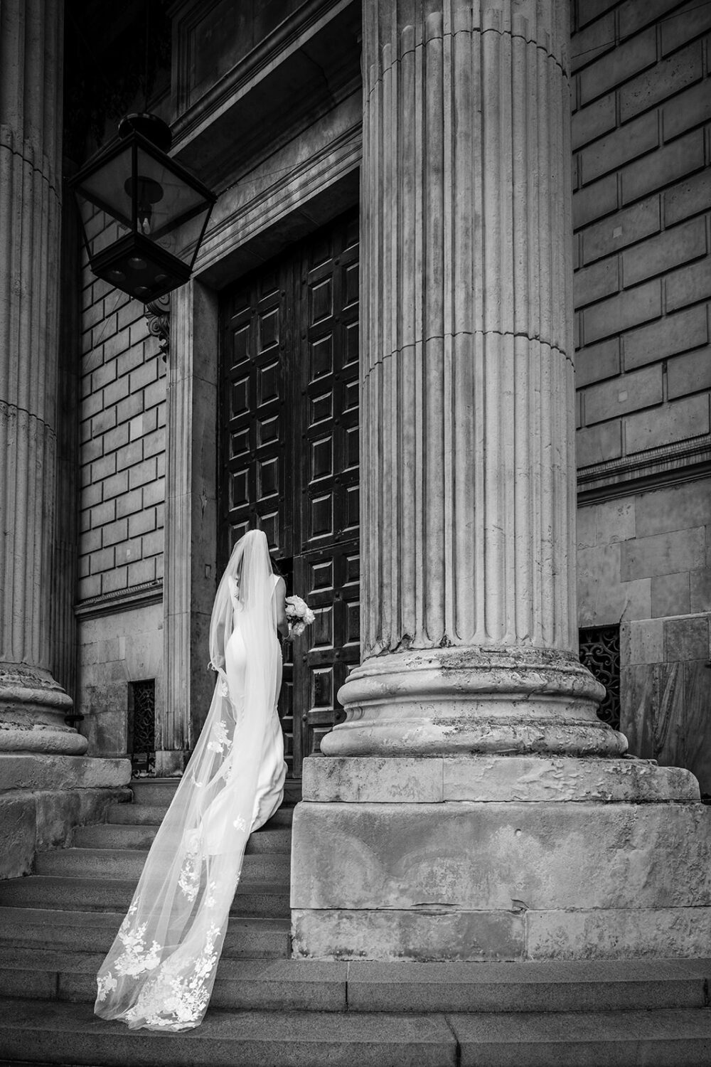 Black and white photo of a bride with a long veil on the steps of St Paul's Cathedral