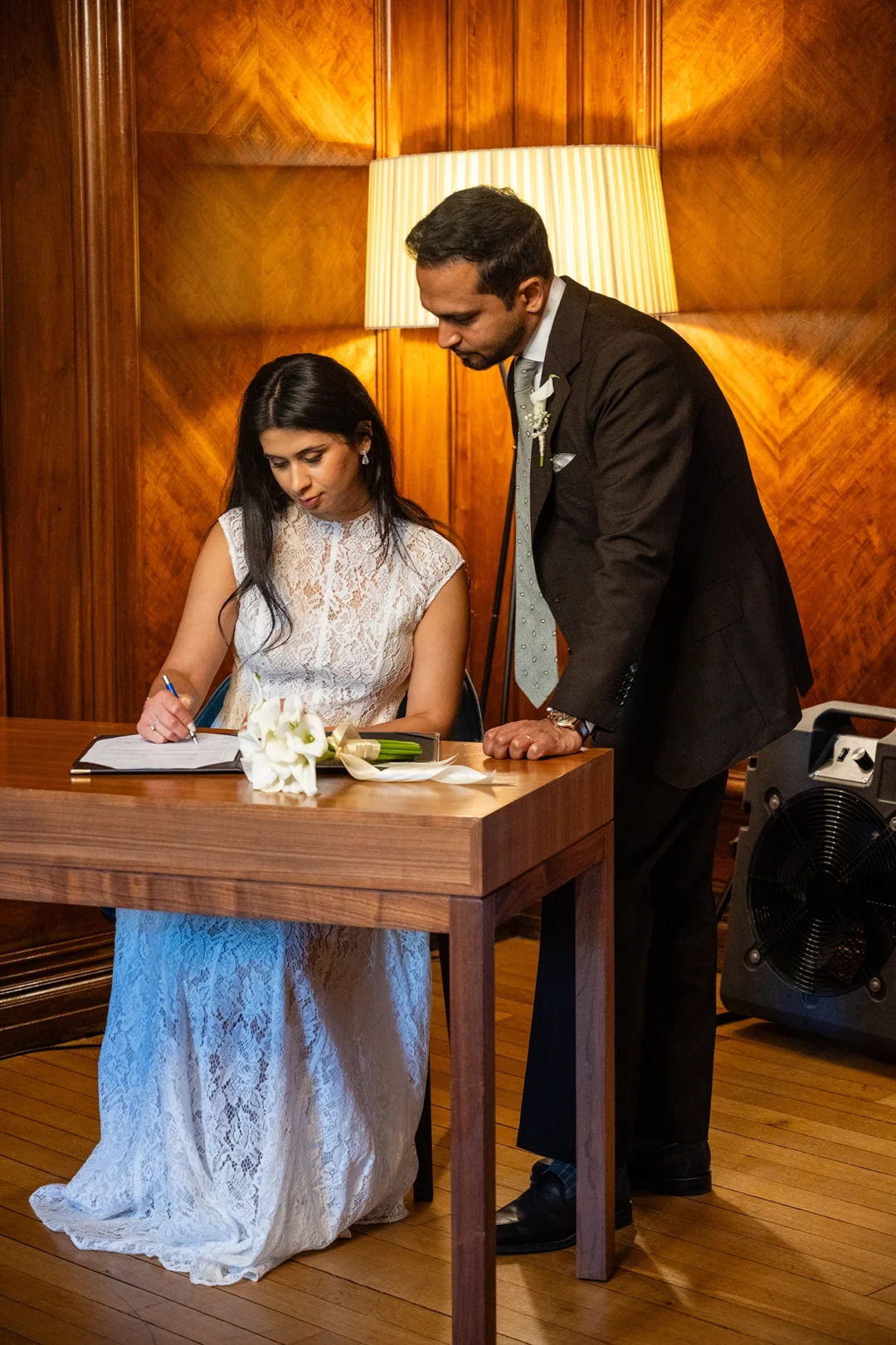 Bride signing the register as the groom looks on