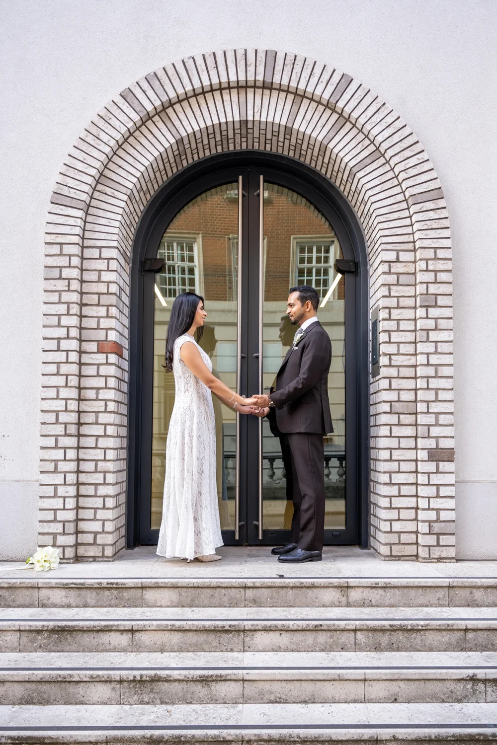 Bride and groom holding hands under a brick arched doorway