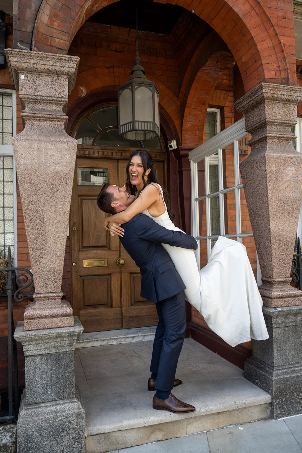 Groom lifting his bride in a stone archway in London