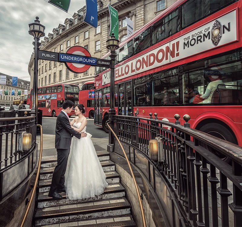 Bride and groom on the steps of a London Underground entrance beside a red bus
