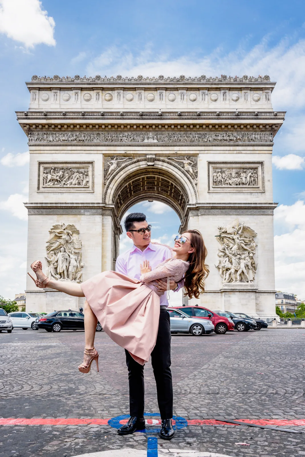 Groom lifting the bride in a pink dress in front of the Arc de Triomphe, Paris pre wedding shoot