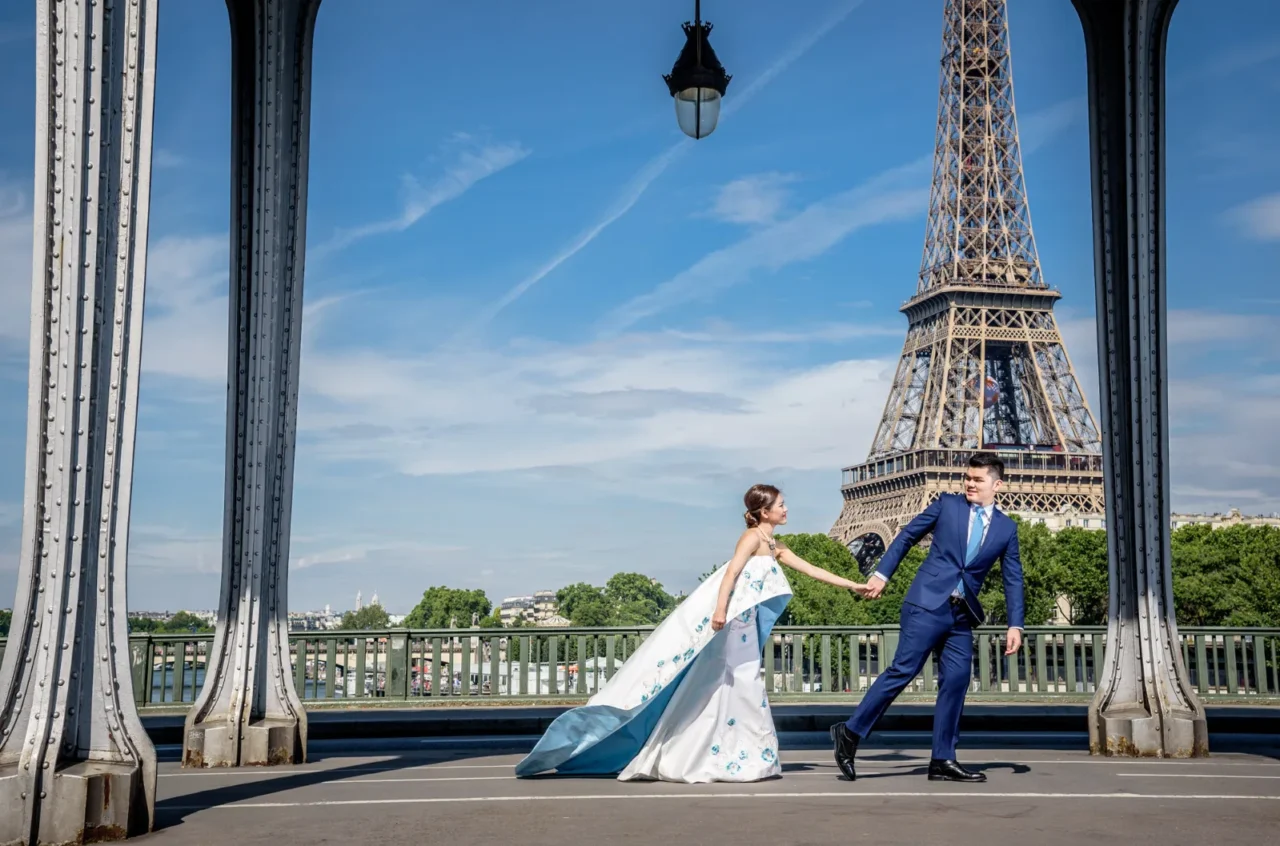 Bride with an embroidered train and groom walking on Pont de Bir-Hakeim towards the Eiffel Tower