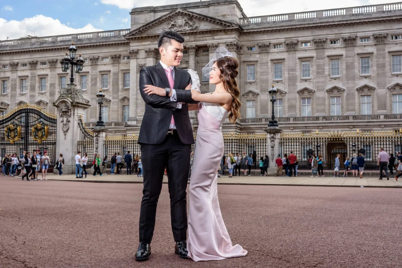 Bride in pale pink gown and groom in front of the Buckingham Palace gates