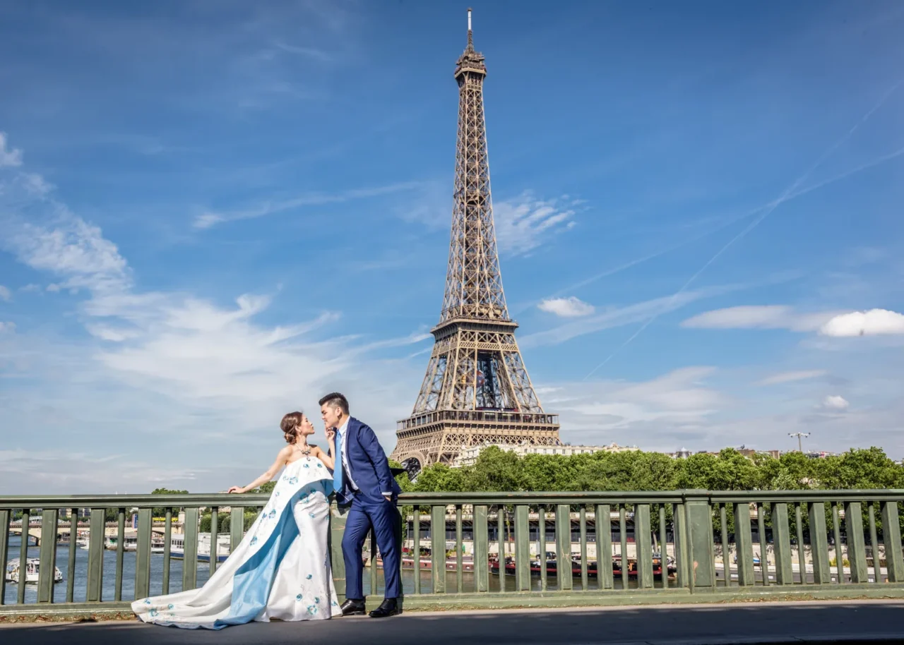 Couple on a Paris bridge railing with the Eiffel Tower behind them