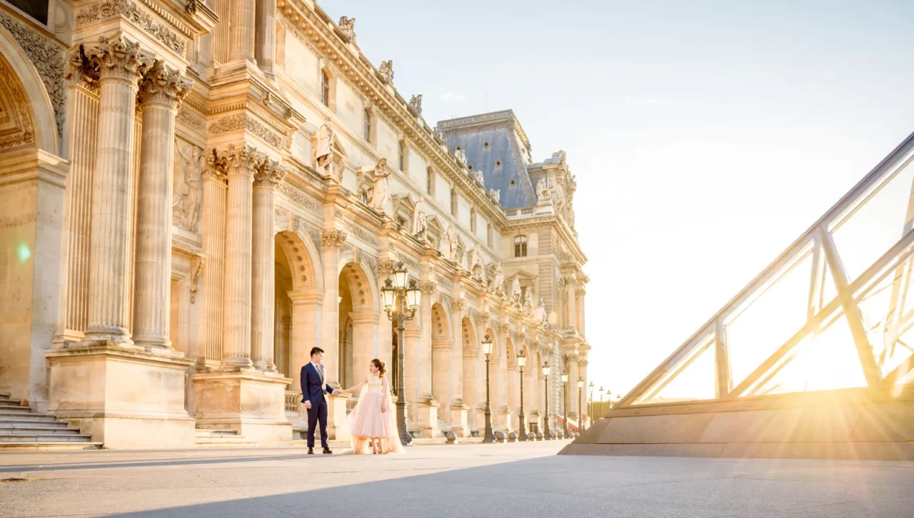 Couple walking in the Louvre courtyard with the sun bursting past the pyramid