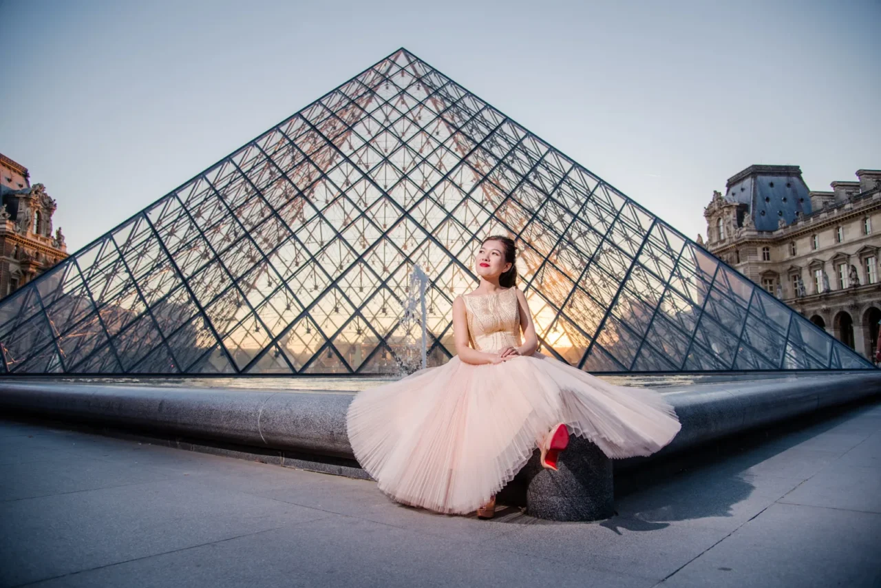 Bride in a pale pink tulle gown sitting in front of the Louvre pyramid