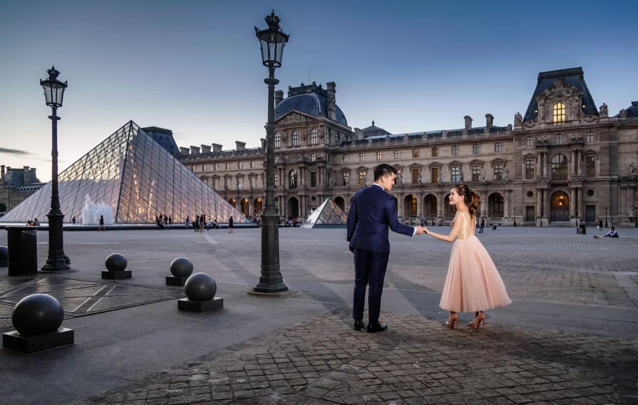 Couple holding hands in the Louvre courtyard with the glass pyramid behind