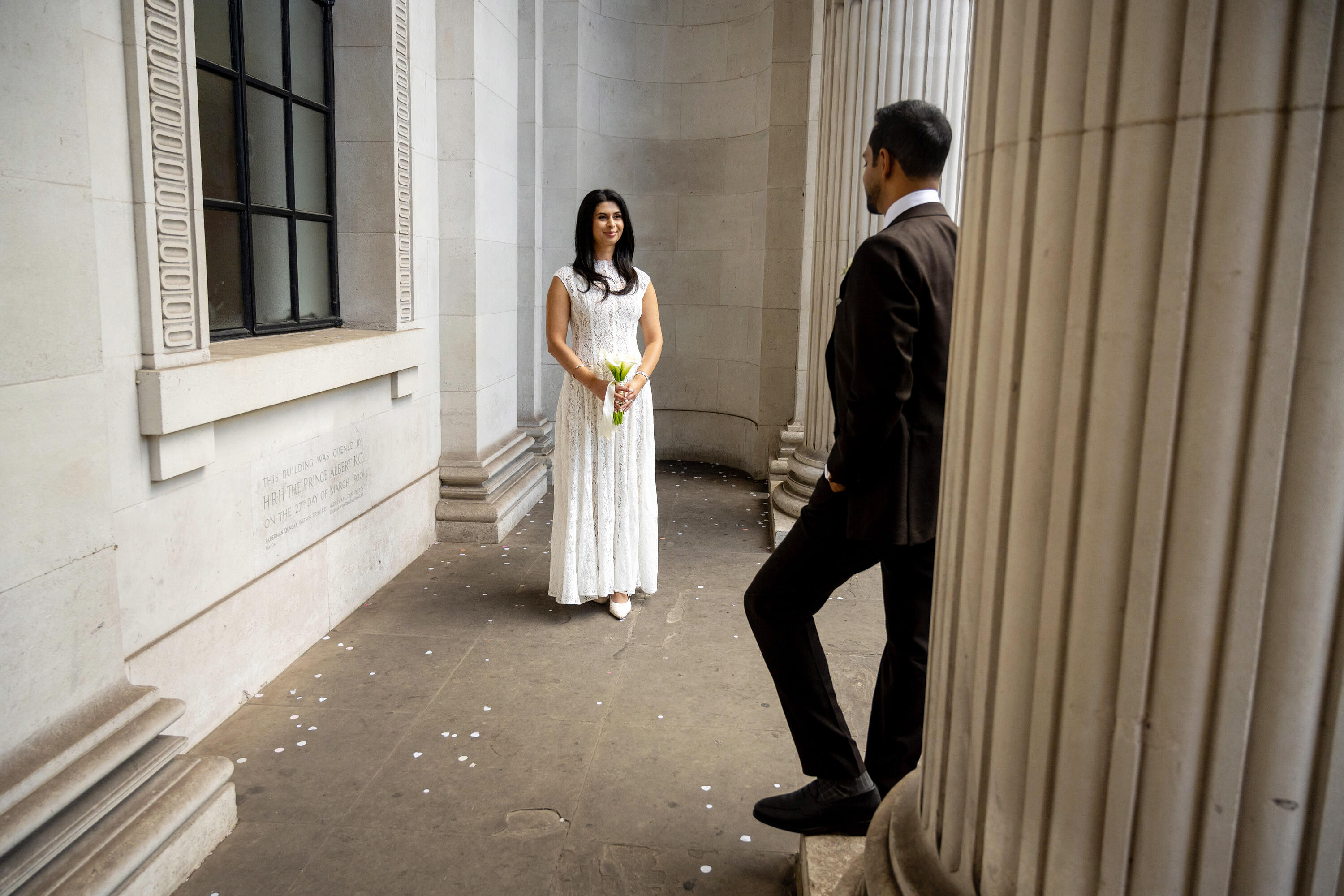 Bride waiting in the colonnade at Old Marylebone Town Hall beside a display of pink peonies
