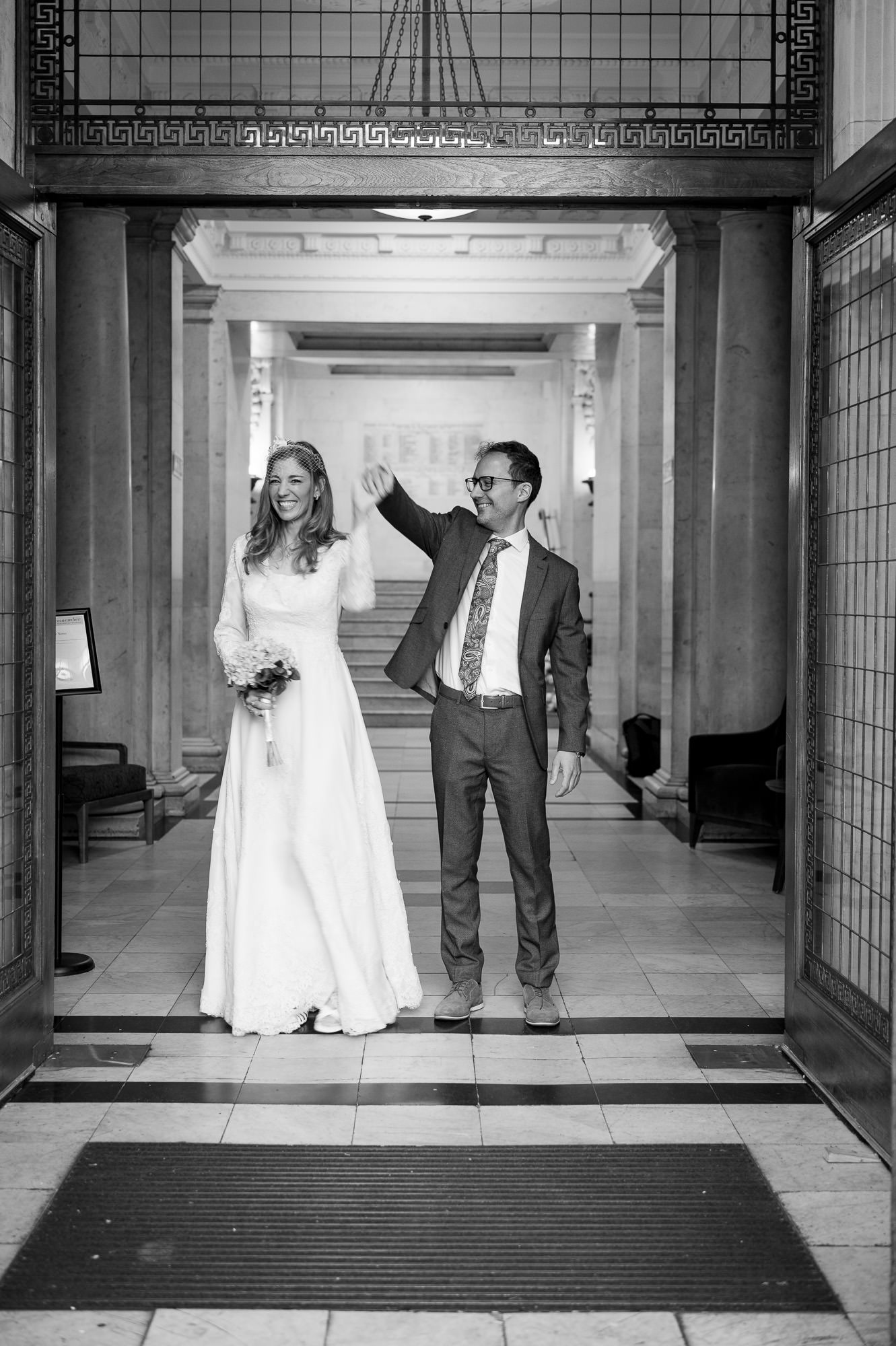 Bride and groom walking out through the doors of Old Marylebone Town Hall, arms raised