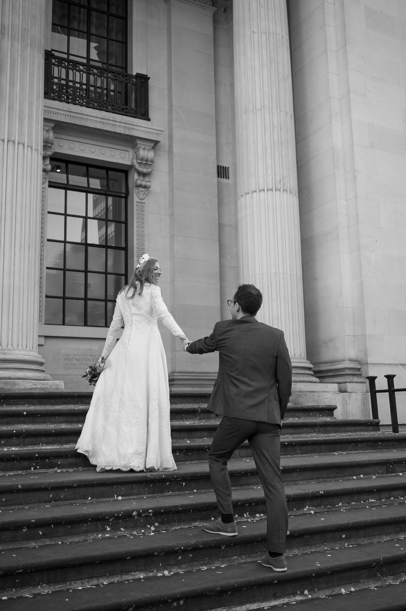 Groom reaching for the bride's hand on the steps of Old Marylebone Town Hall
