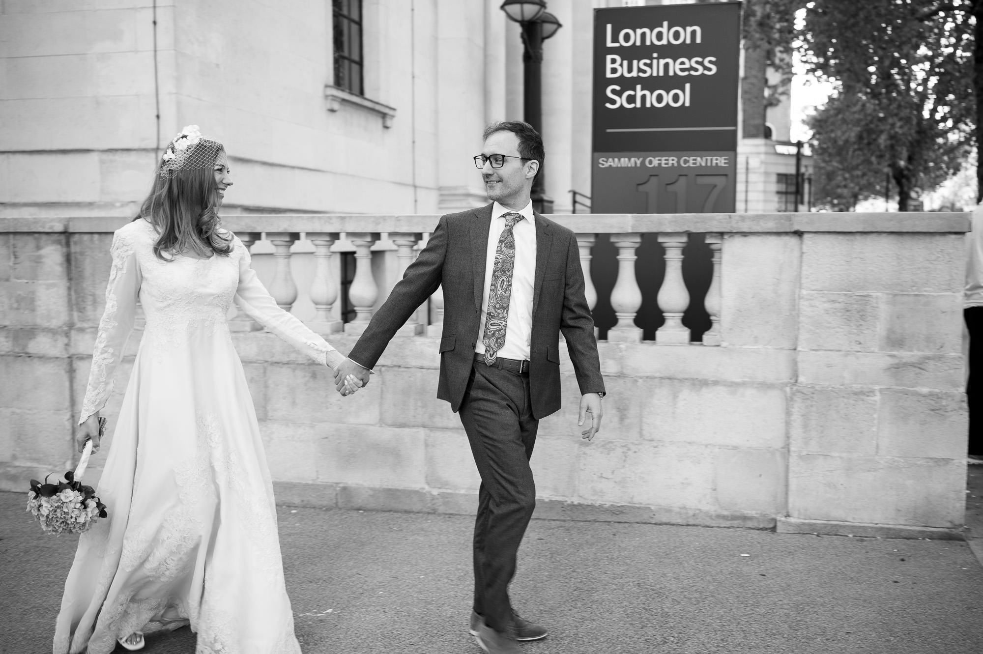 Bride and groom walking hand in hand past London Business School