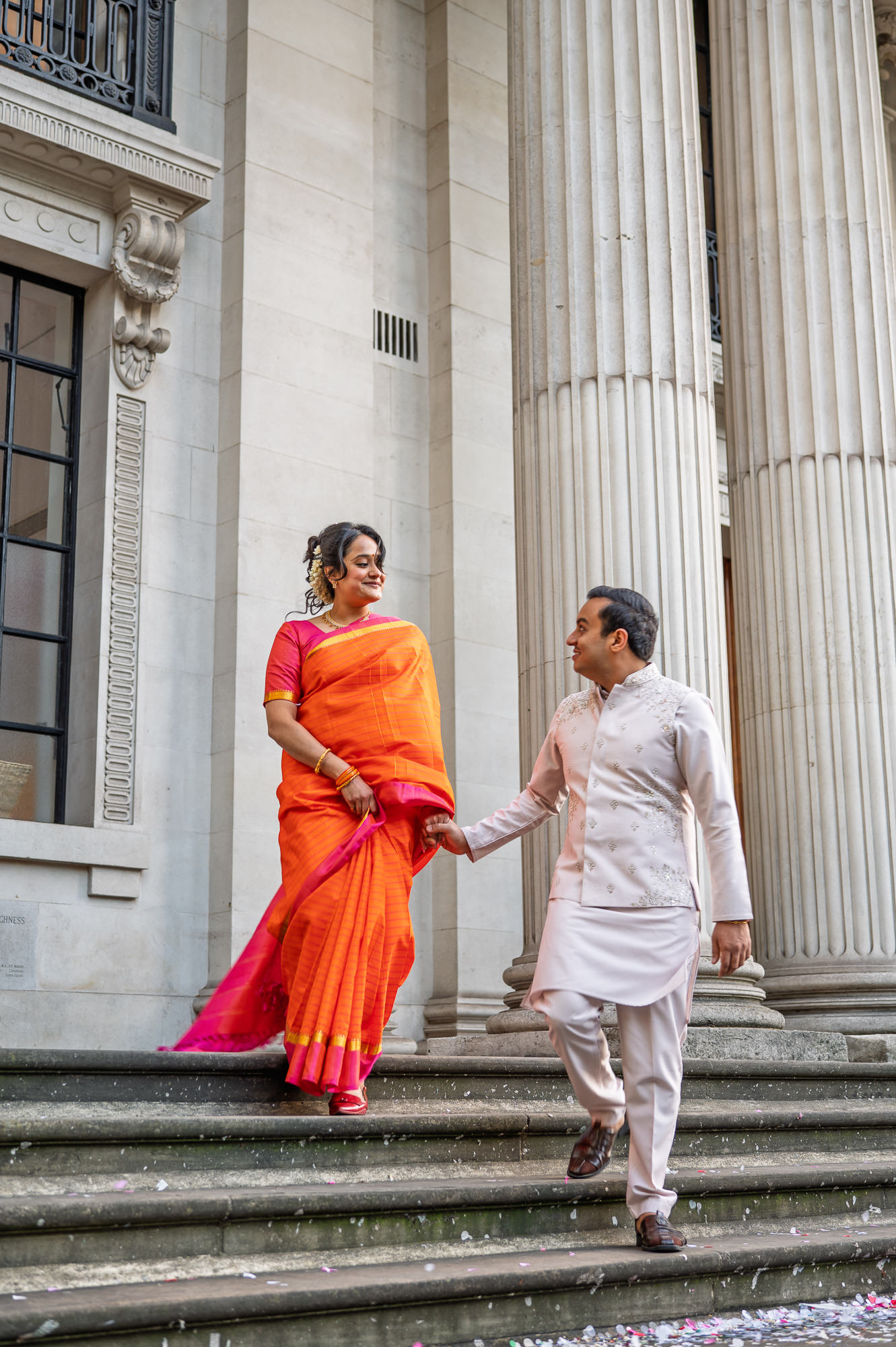 Bride in an orange silk sari and groom walking down the steps of Old Marylebone Town Hall