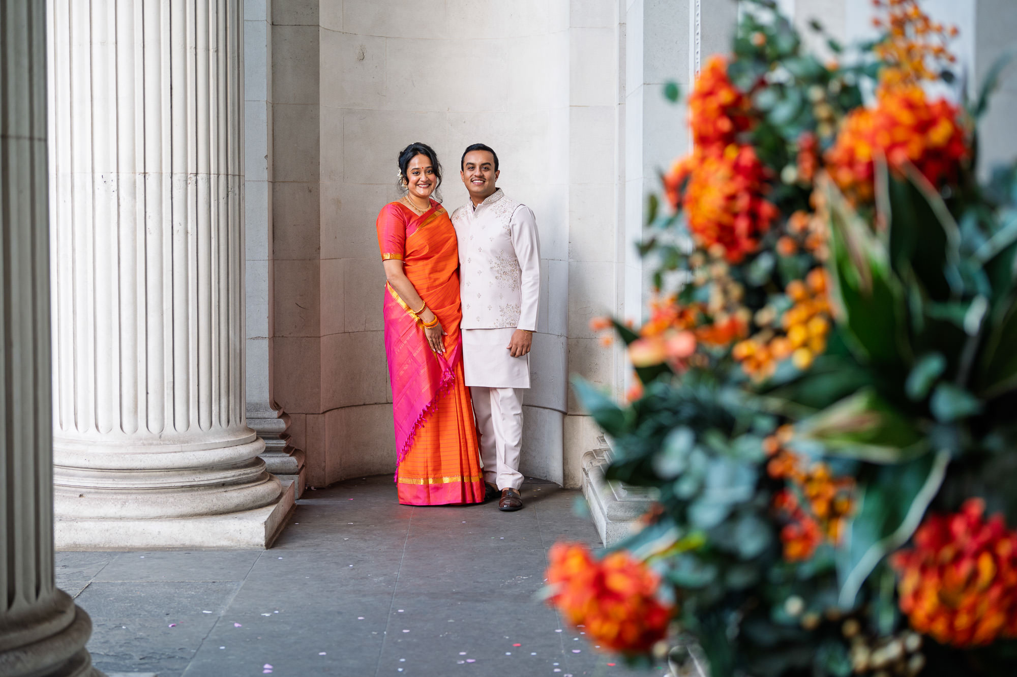 Bride and groom between the columns at Old Marylebone Town Hall with orange flowers in the foreground