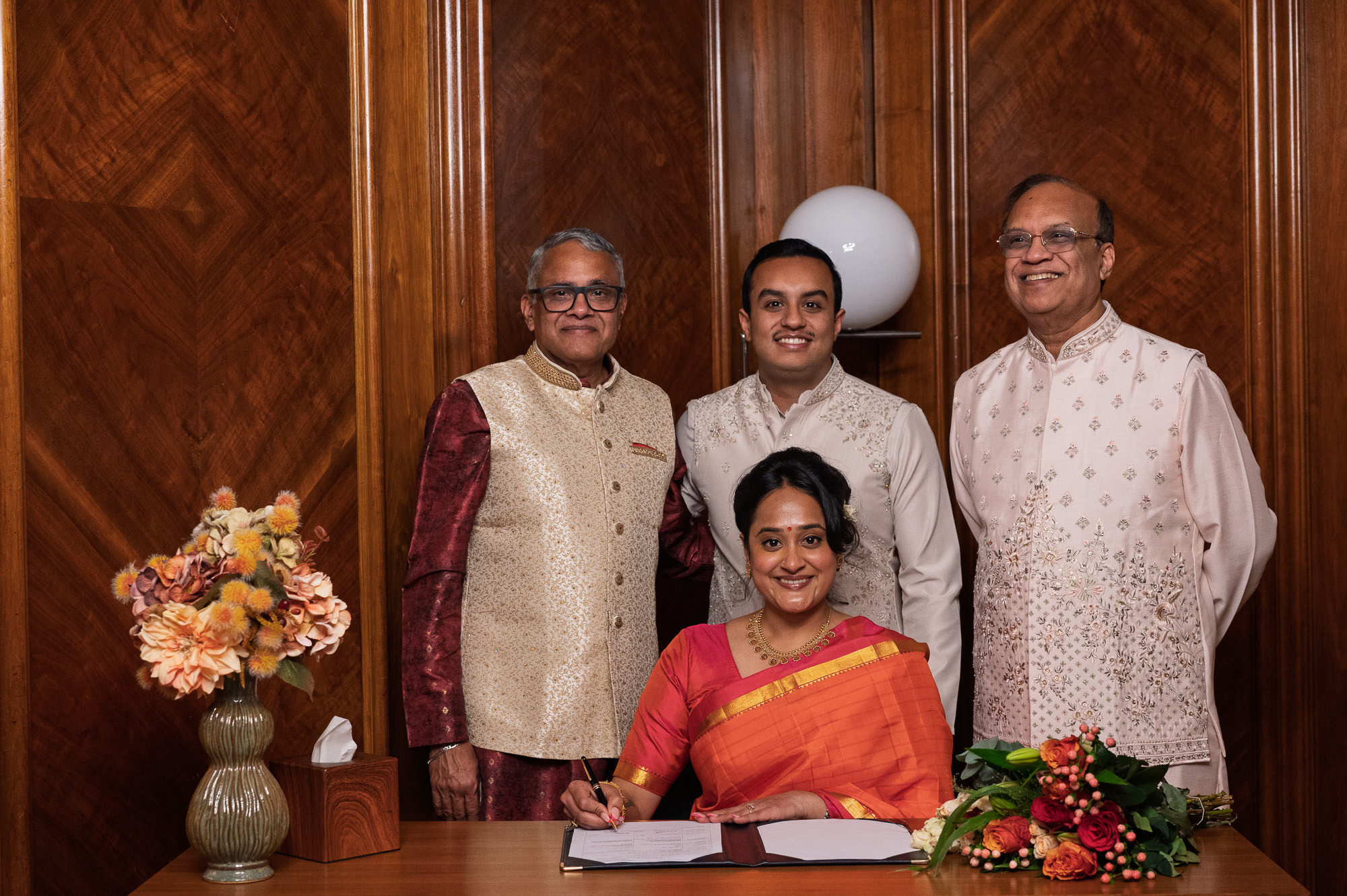 Bride signing the register with the groom and family behind her