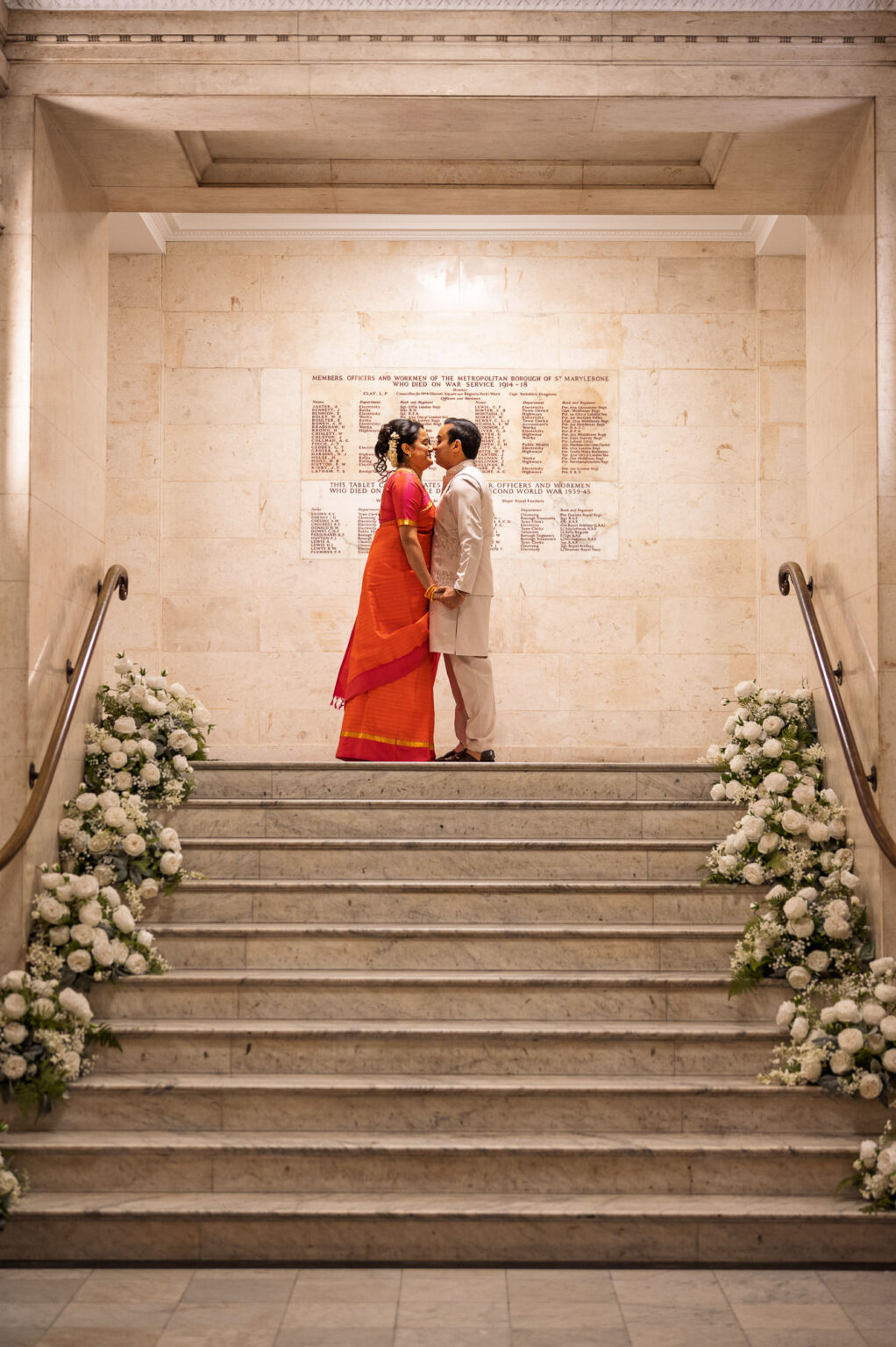 Bride and groom at the top of the flower-lined staircase at Old Marylebone Town Hall at night
