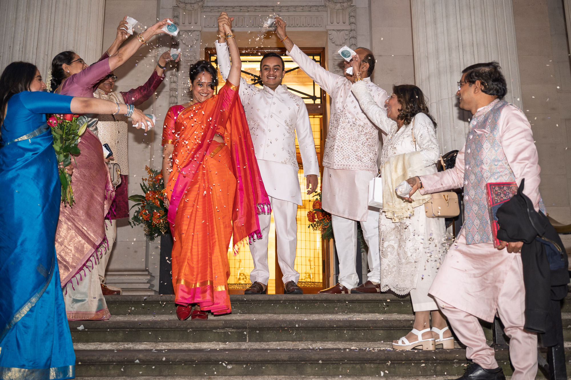 Family throwing confetti over the bride and groom on the steps of Old Marylebone Town Hall at night