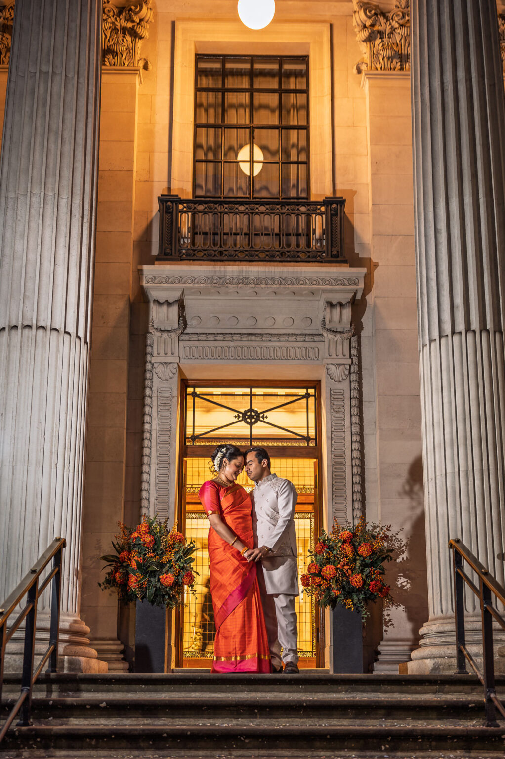 Bride and groom in the lit doorway of Old Marylebone Town Hall after dark