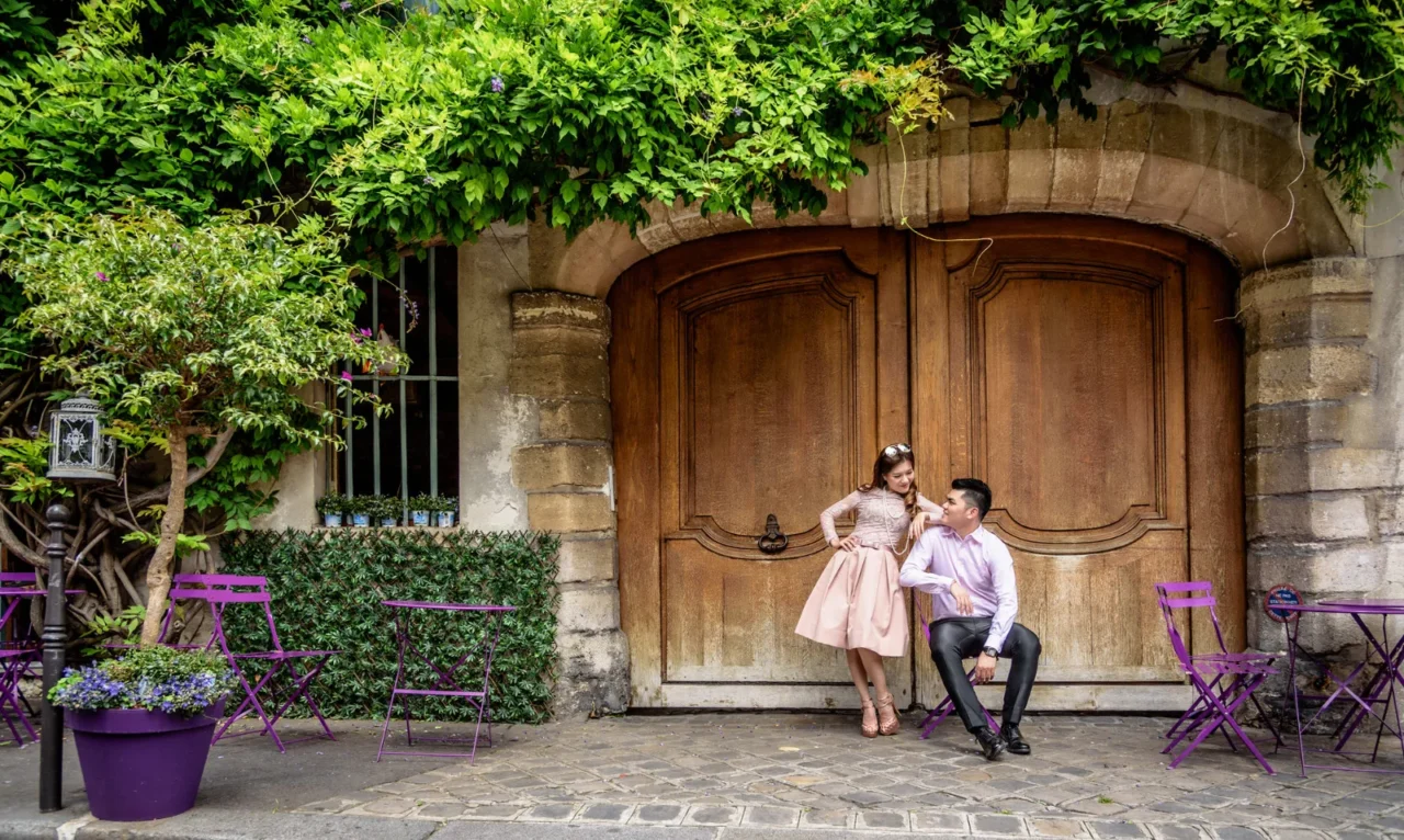 Couple sitting outside a wooden doorway at a Paris cafe with purple chairs