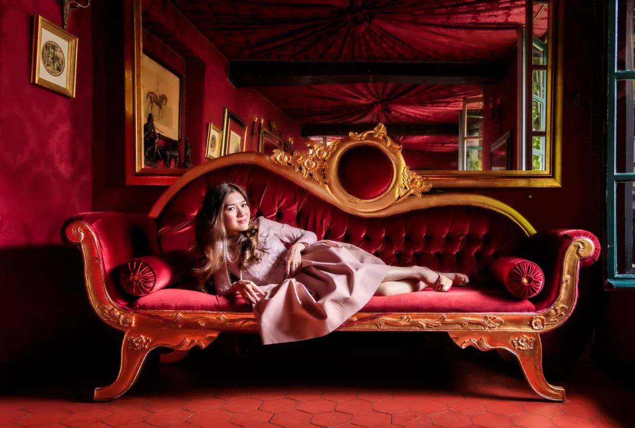 Bride in a pink dress lying on a red velvet chaise inside a Paris cafe