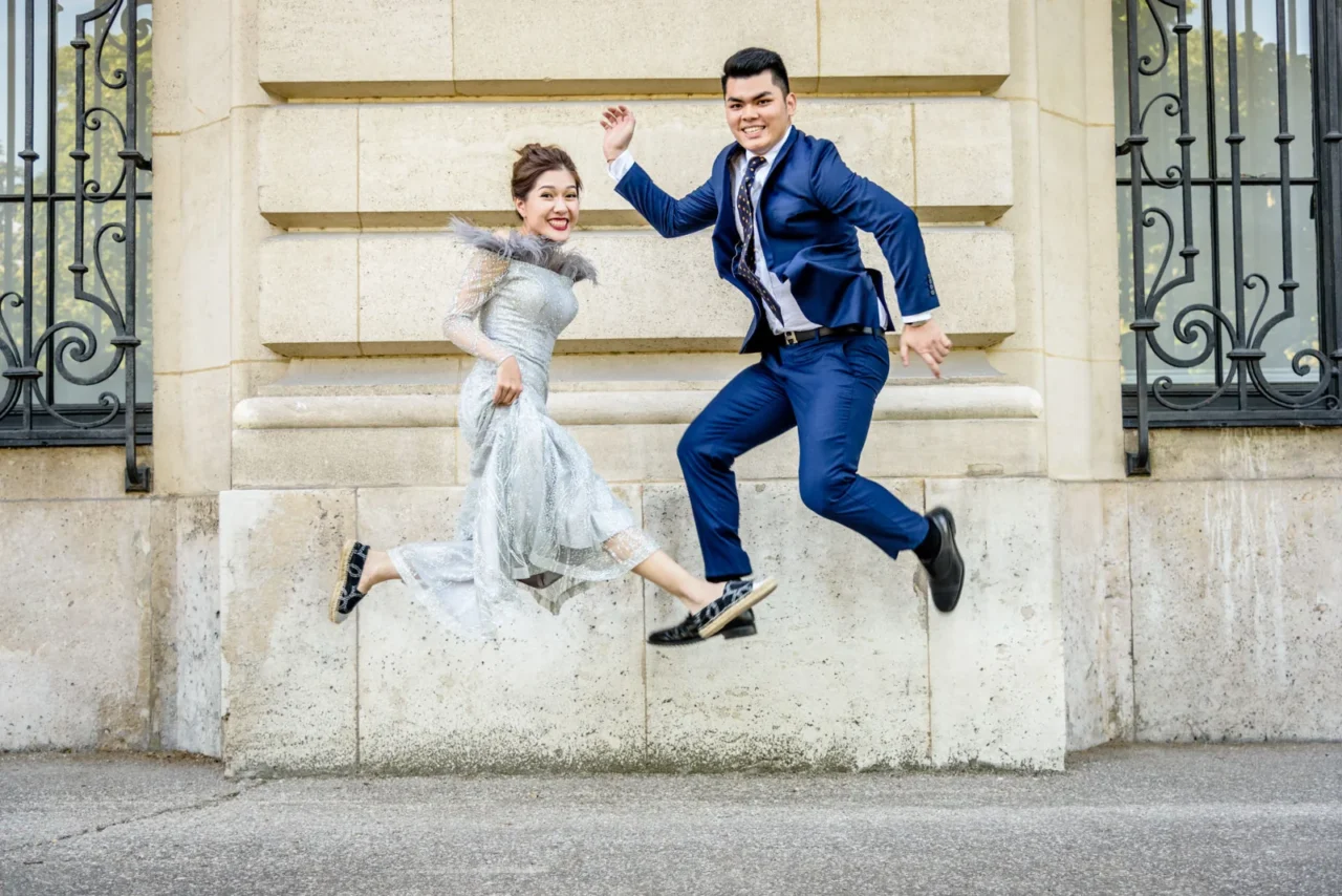 Bride and groom jumping in front of a Parisian stone wall and iron gates