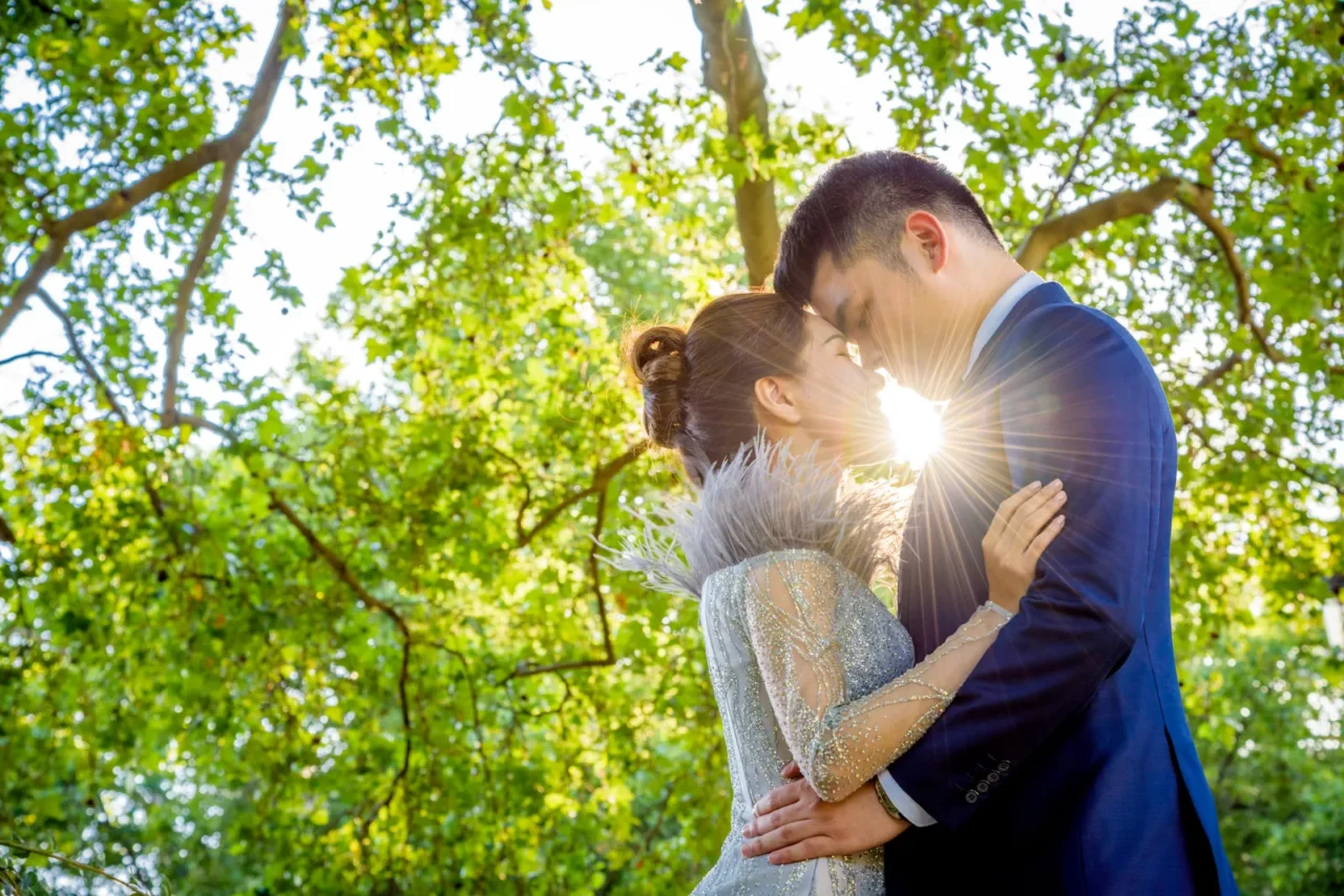 Couple embracing under green trees with the sun shining through, Paris