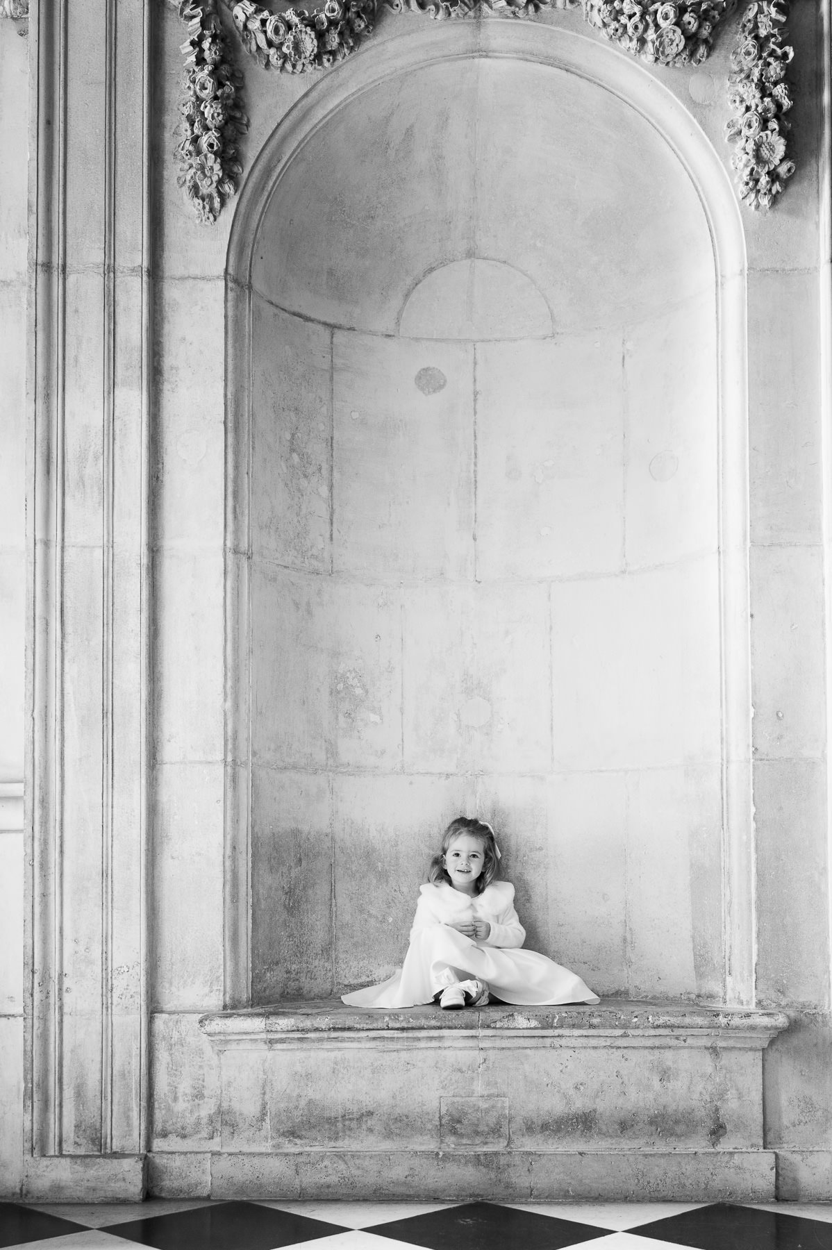 Black and white photo of a little girl sitting in a stone alcove inside St Paul's Cathedral