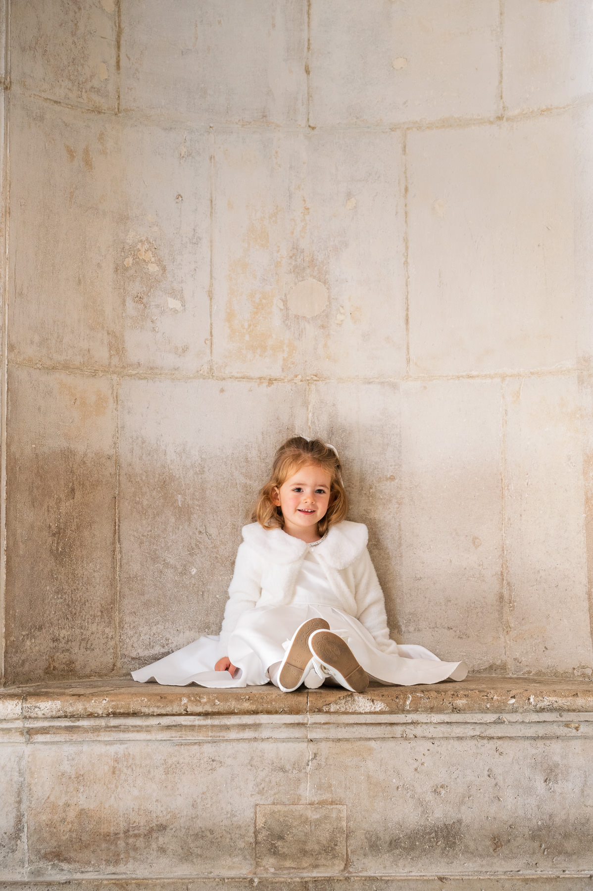 Little girl in a white christening outfit sitting in a stone niche at St Paul's Cathedral