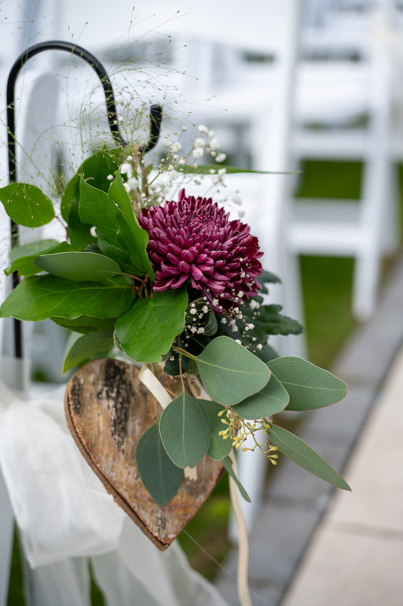 Flowers in a wooden heart hanging from a shepherd's crook beside the ceremony chairs at Selden Barns
