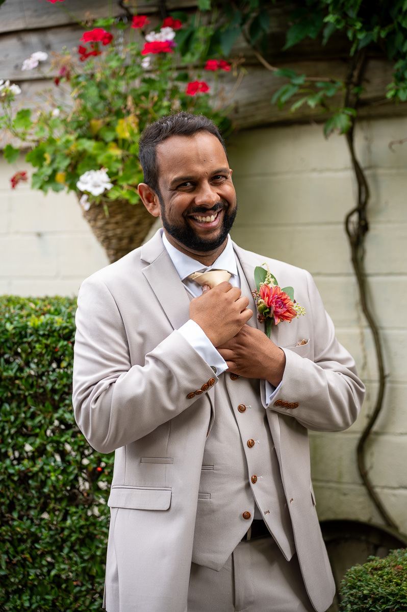 The groom laughing outside before the ceremony, in a stone-coloured three-piece suit