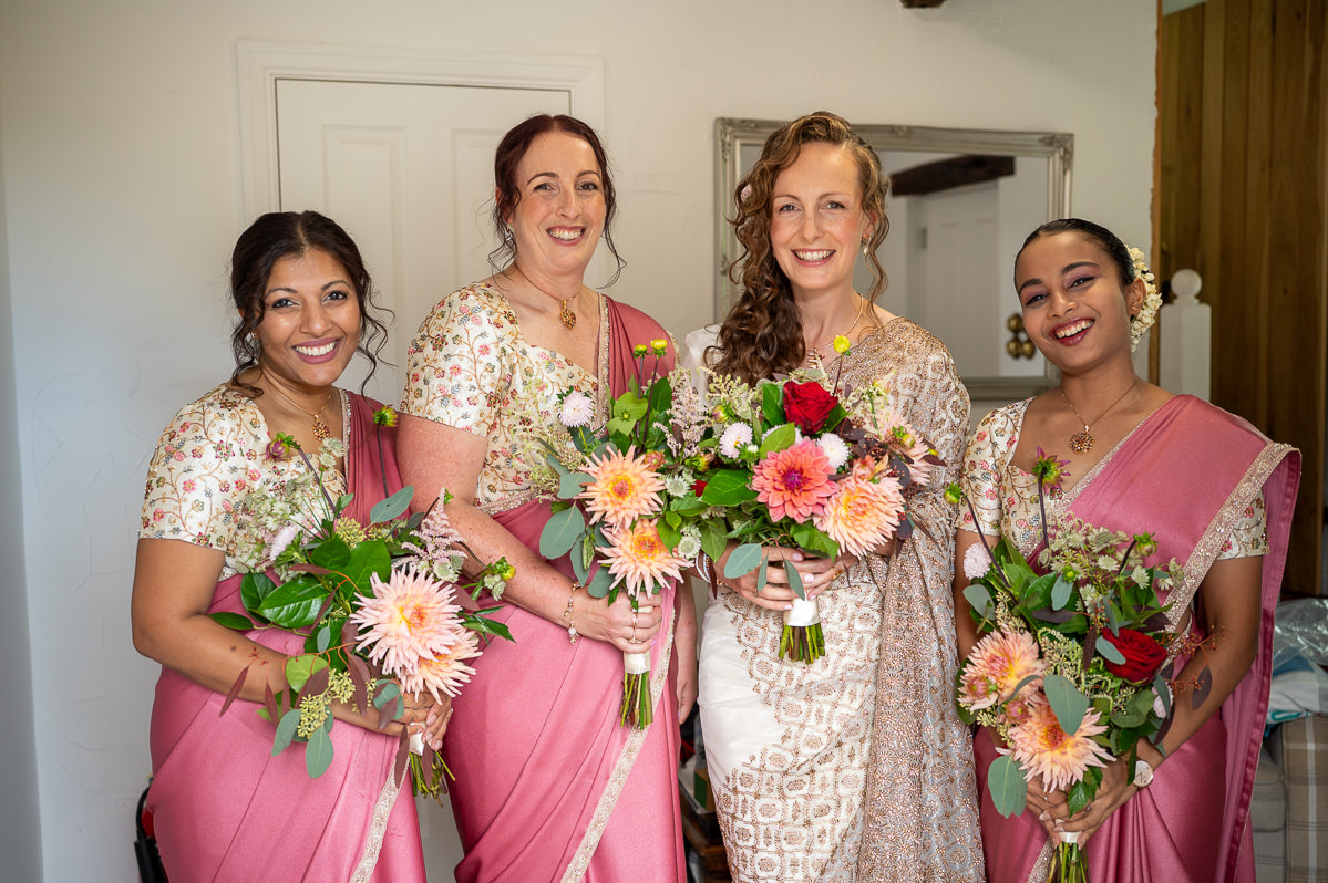 The bride with her three bridesmaids in pink sarees, holding dahlia bouquets
