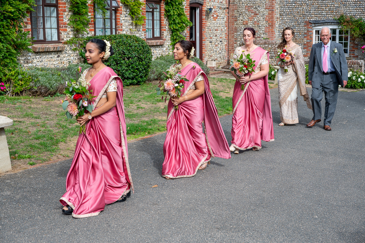 Bridesmaids in pink sarees walking to the ceremony at Selden Barns