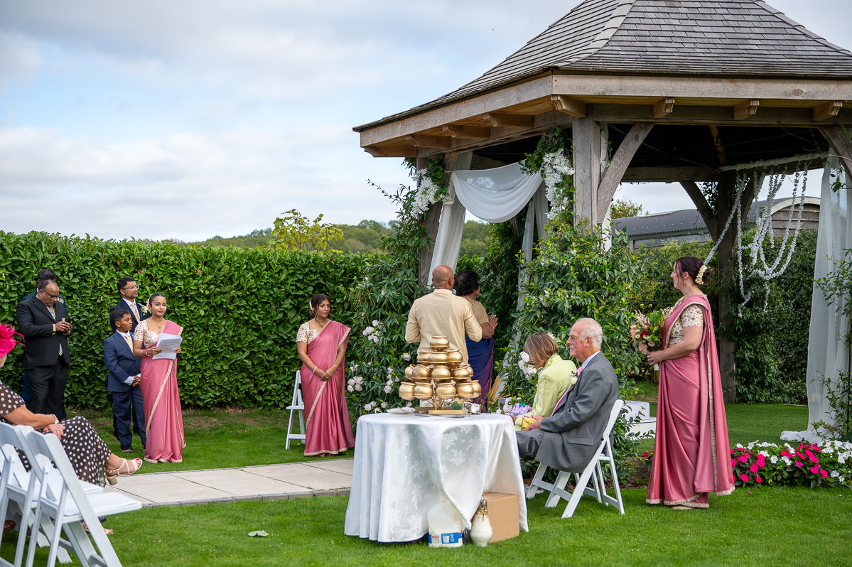 The oak pergola at Selden Barns set for the Sri Lankan ceremony, the gold milk pots on a table beside it